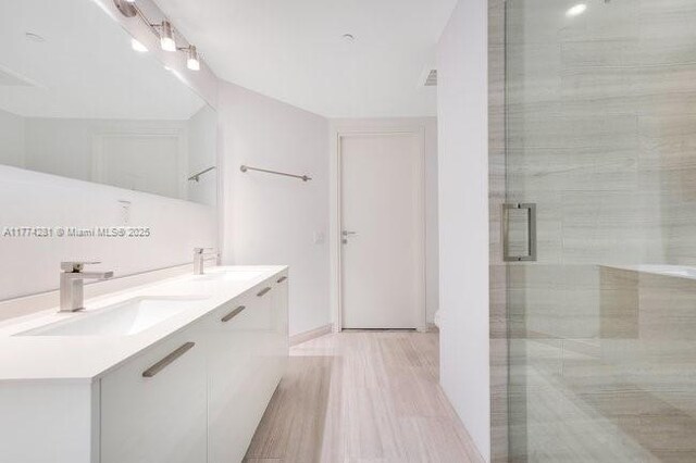 1300 Brickell Bay Dr Unit 601, Miami, FL 33131 - full bathroom with double vanity, a shower stall, a sink, and wood finished floors