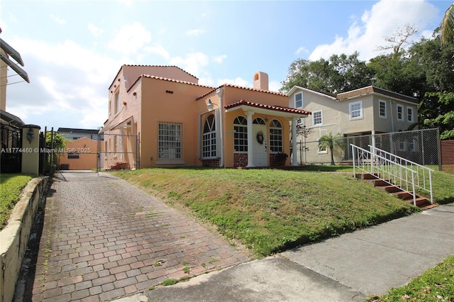 mediterranean / spanish home featuring stucco siding, driveway, a front yard, a tile roof, and a gate