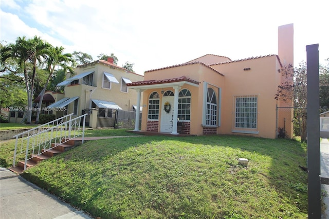 mediterranean / spanish-style home with a tile roof, a front lawn, fence, and stucco siding