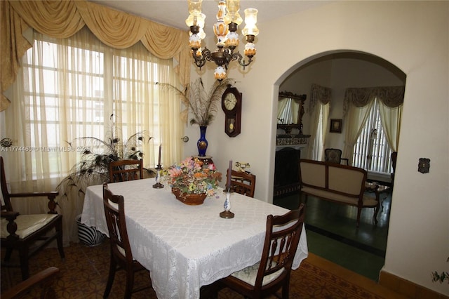dining room with arched walkways, an inviting chandelier, and a fireplace