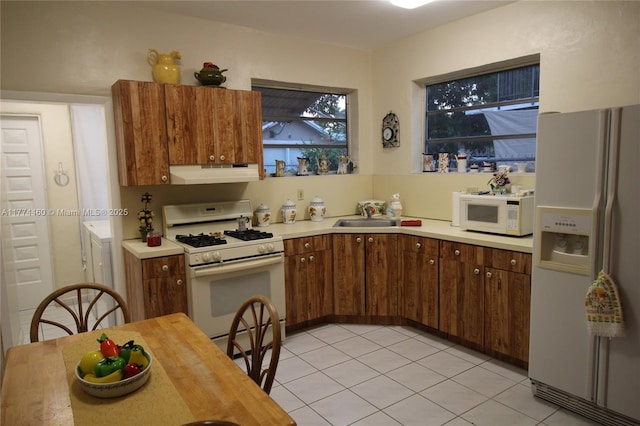 kitchen featuring light tile patterned floors, white appliances, under cabinet range hood, a sink, and light countertops