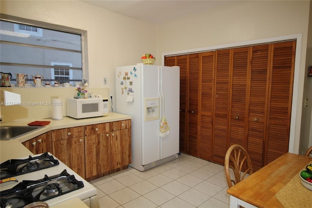 kitchen featuring white appliances, brown cabinetry, light tile patterned flooring, a sink, and light countertops