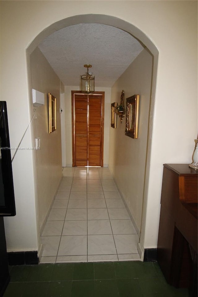 corridor with light tile patterned floors, arched walkways, and a textured ceiling