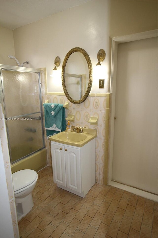 bathroom with toilet, vanity, a wainscoted wall, and enclosed tub / shower combo