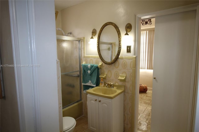 bathroom featuring toilet, tile walls, enclosed tub / shower combo, wainscoting, and vanity