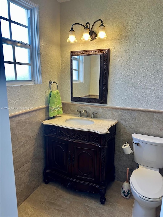 bathroom featuring toilet, vanity, wainscoting, and tile walls