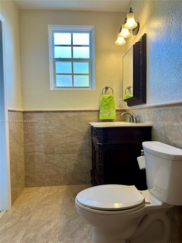 bathroom with toilet, tile walls, vanity, and wainscoting
