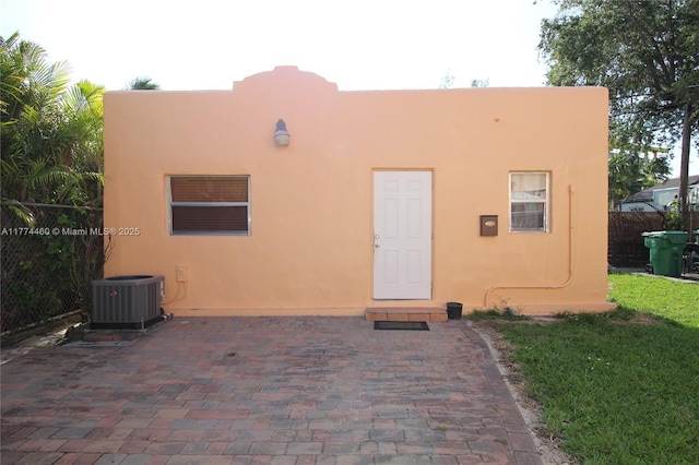 rear view of house with central AC unit, fence, a patio area, and stucco siding