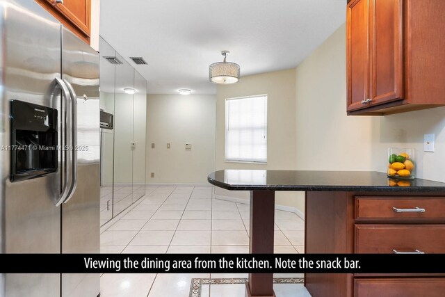 kitchen with visible vents, brown cabinets, dark countertops, stainless steel fridge with ice dispenser, and light tile patterned floors