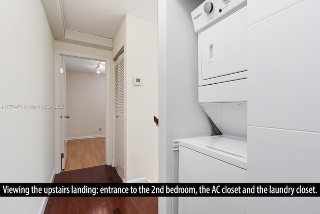 washroom featuring baseboards, wood finished floors, stacked washer / drying machine, and laundry area