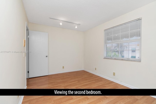 unfurnished room featuring light wood-style flooring, rail lighting, baseboards, and a textured ceiling
