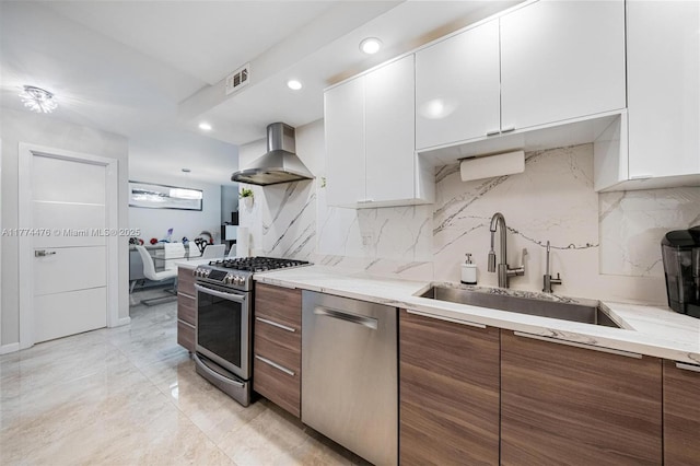 kitchen with wall chimney range hood, white cabinetry, visible vents, a sink, and stainless steel appliances