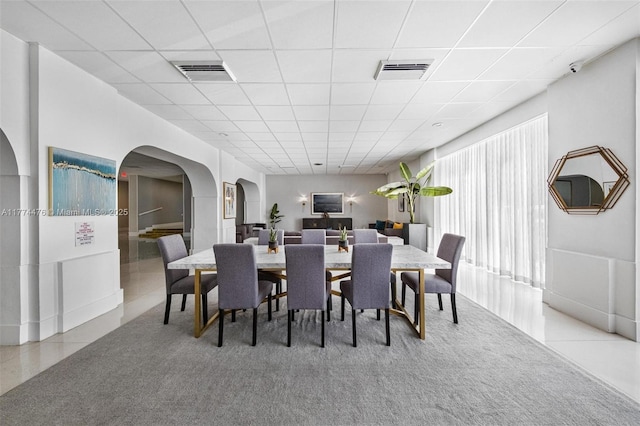 tiled dining area featuring visible vents, arched walkways, and a drop ceiling