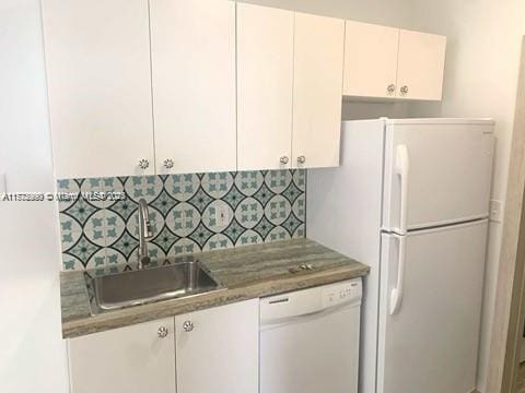 kitchen featuring a sink, white cabinets, tasteful backsplash, and white appliances