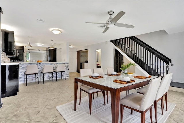dining room featuring light tile patterned floors, a ceiling fan, visible vents, and stairs