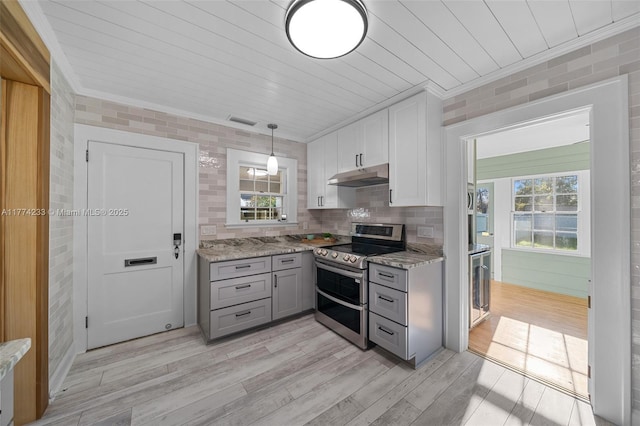 kitchen with double oven range, under cabinet range hood, gray cabinets, ornamental molding, and light wood-style floors