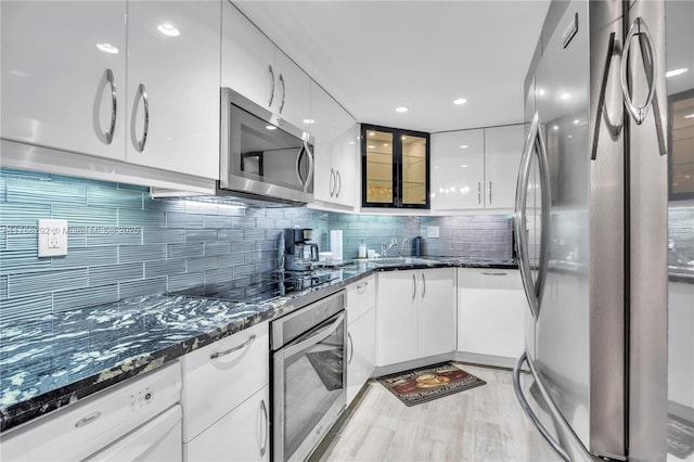 kitchen featuring stainless steel appliances, modern cabinets, dark stone counters, decorative backsplash, and white cabinetry