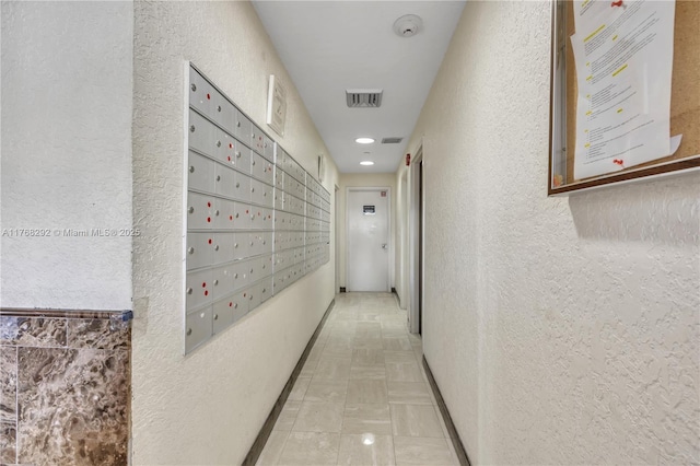 hall with a textured wall, mail area, visible vents, and recessed lighting