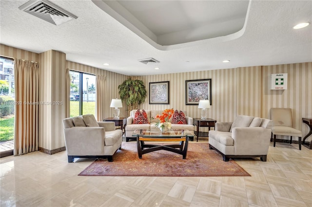 living area with wallpapered walls, visible vents, and a textured ceiling