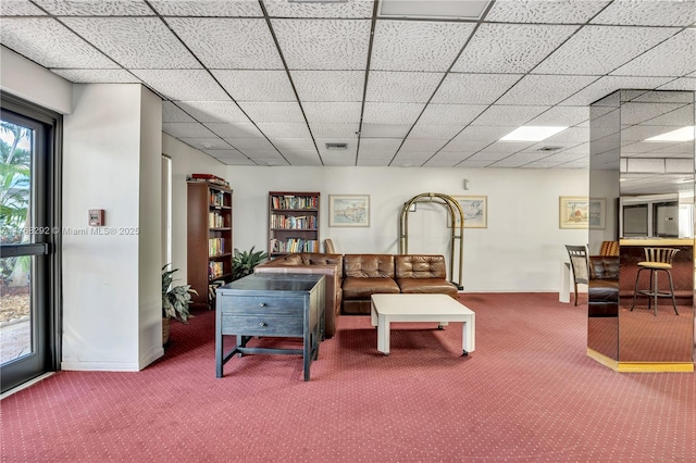 carpeted living room featuring baseboards and a drop ceiling
