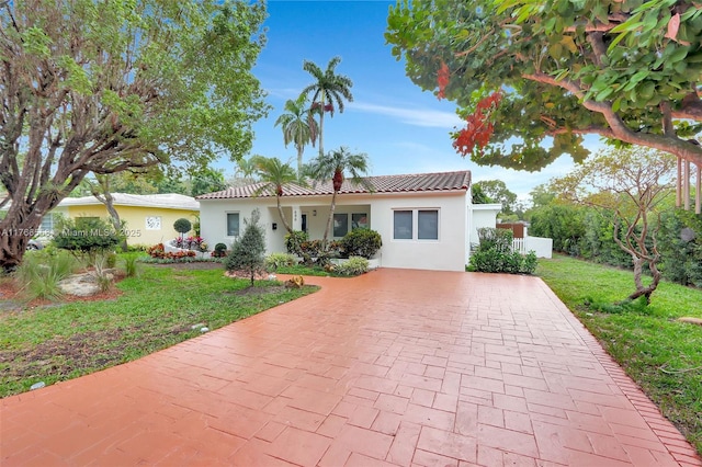 mediterranean / spanish-style home with stucco siding, driveway, a tiled roof, and a front lawn