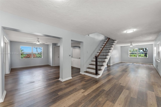 unfurnished living room featuring a ceiling fan, dark wood-style flooring, stairway, and a textured ceiling