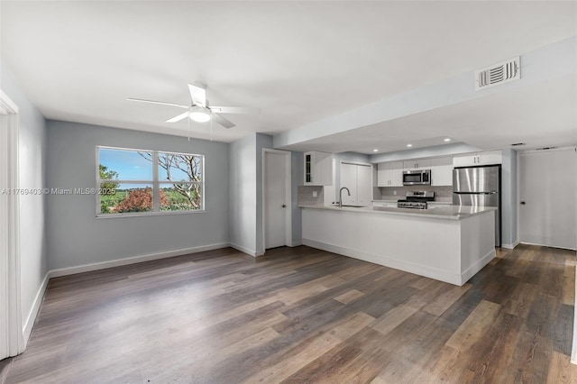 kitchen with a sink, appliances with stainless steel finishes, a peninsula, dark wood-style floors, and visible vents