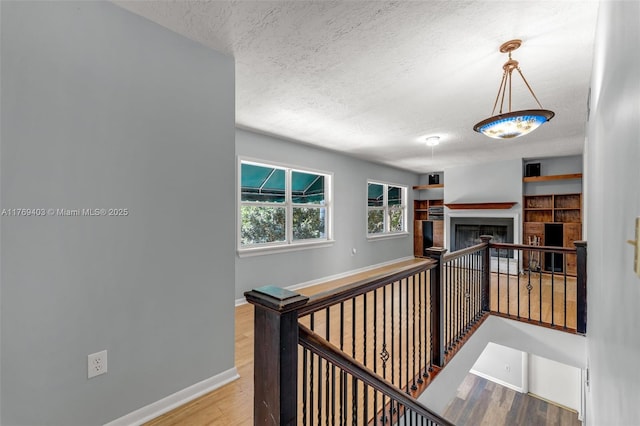 hall with baseboards, an upstairs landing, wood finished floors, and a textured ceiling