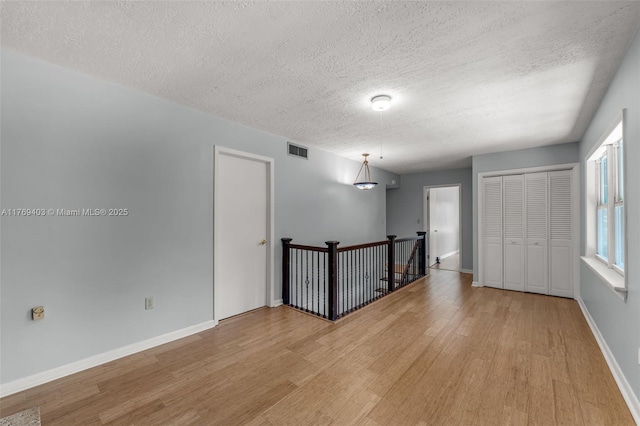 unfurnished room with baseboards, a textured ceiling, visible vents, and light wood finished floors