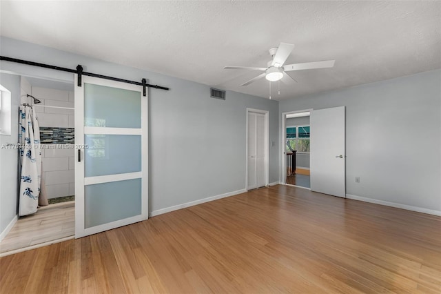 empty room with a ceiling fan, visible vents, a barn door, and wood finished floors