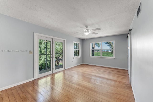 spare room with a textured ceiling, visible vents, light wood finished floors, baseboards, and ceiling fan