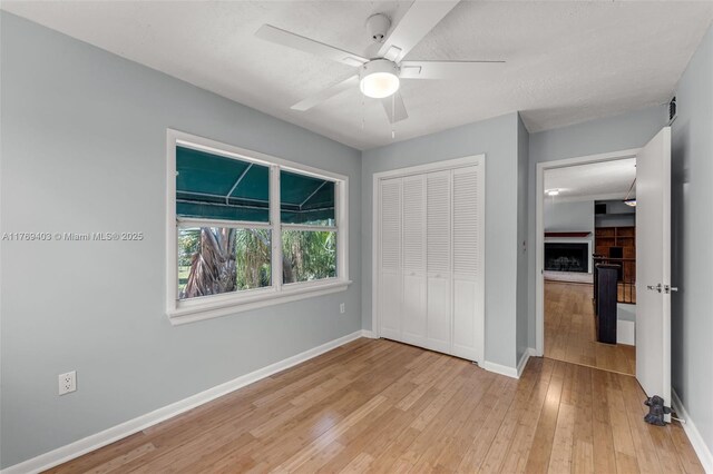unfurnished bedroom with baseboards, light wood-style floors, ceiling fan, a closet, and a fireplace