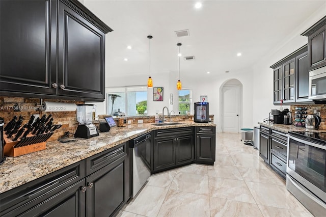 kitchen with stainless steel appliances, arched walkways, dark cabinets, and a sink