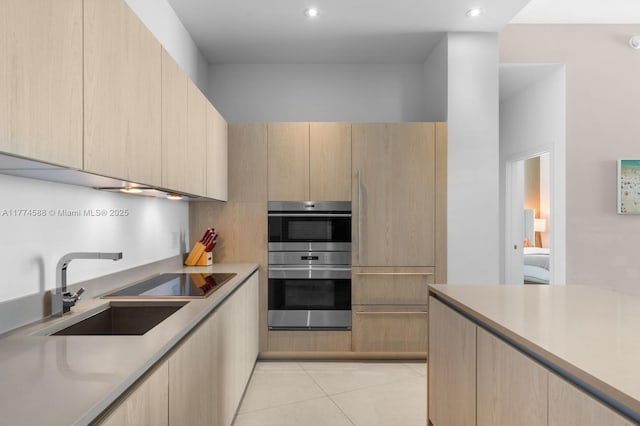 kitchen featuring light countertops, stainless steel double oven, a sink, modern cabinets, and light brown cabinets