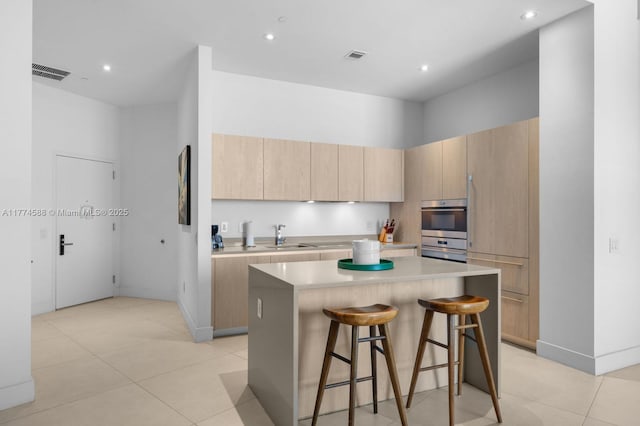 kitchen featuring light countertops, a breakfast bar, light brown cabinetry, a center island, and visible vents