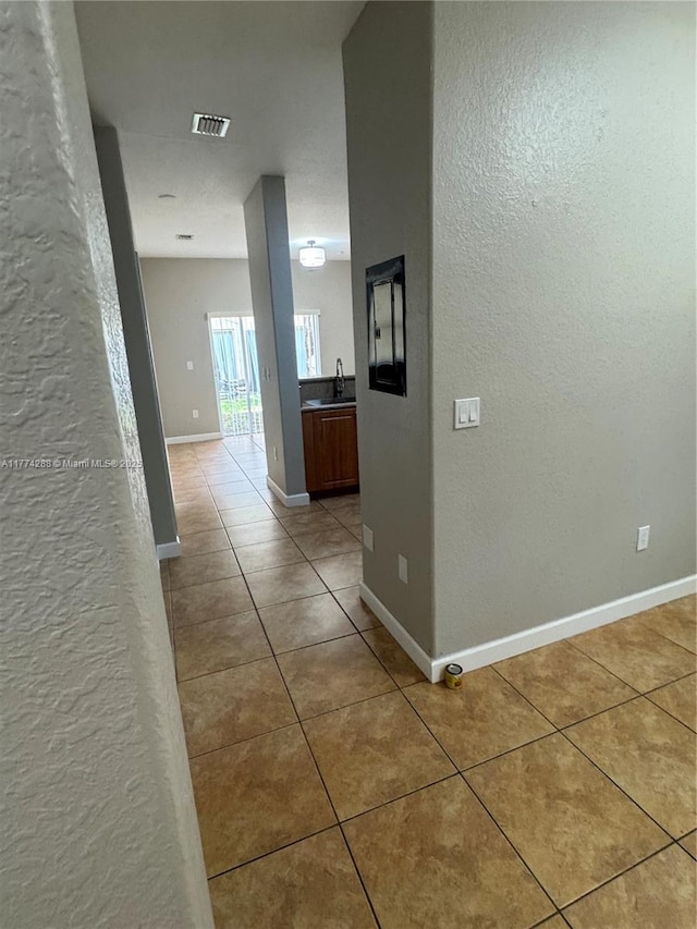 hallway with light tile patterned floors, a sink, baseboards, and visible vents