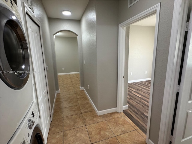 washroom featuring stacked washing maching and dryer, light tile patterned floors, baseboards, visible vents, and arched walkways