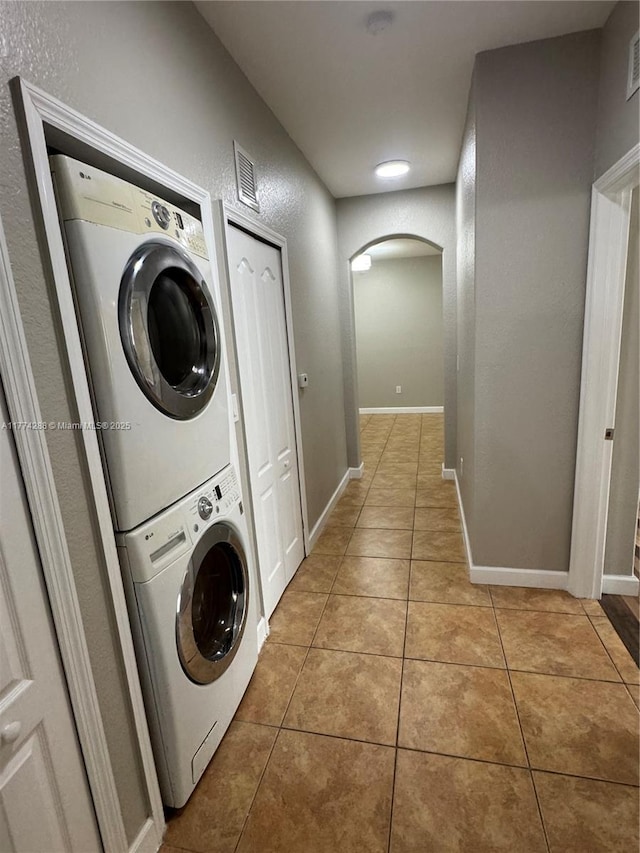 laundry room with stacked washer and dryer, light tile patterned flooring, laundry area, visible vents, and arched walkways