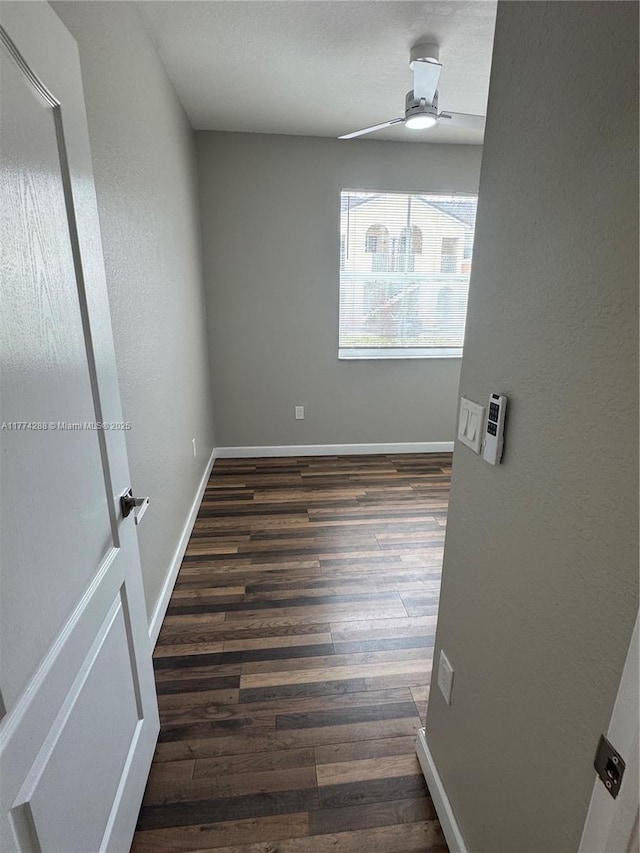 empty room with a ceiling fan, dark wood-style flooring, and baseboards