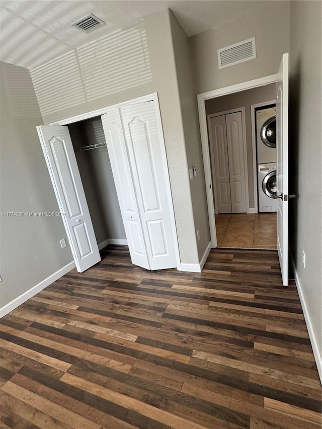 unfurnished bedroom featuring stacked washer and dryer, baseboards, dark wood-style floors, and visible vents