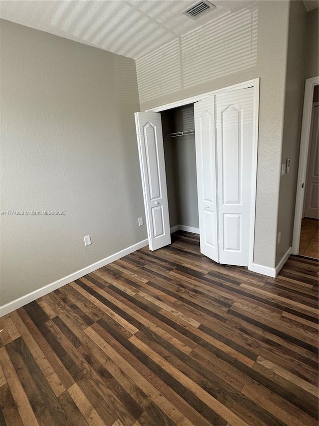 unfurnished bedroom with baseboards, dark wood-style floors, visible vents, and a closet