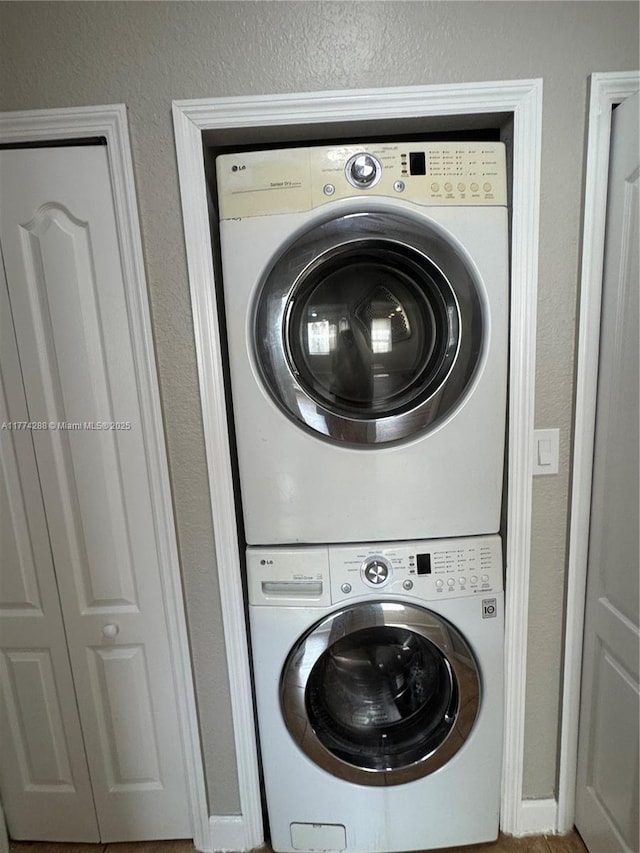 laundry area with stacked washer and clothes dryer, a textured wall, and laundry area