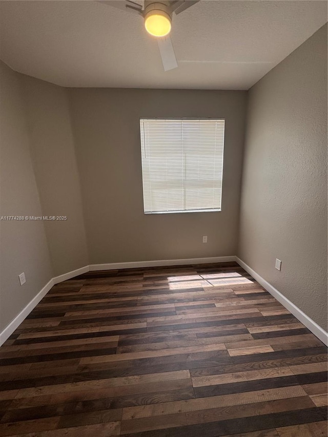 empty room featuring baseboards, dark wood-style flooring, and a ceiling fan