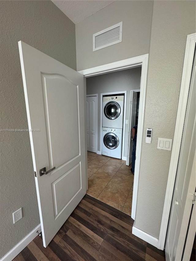 laundry area featuring laundry area, stacked washer / dryer, visible vents, a textured wall, and dark wood-style flooring