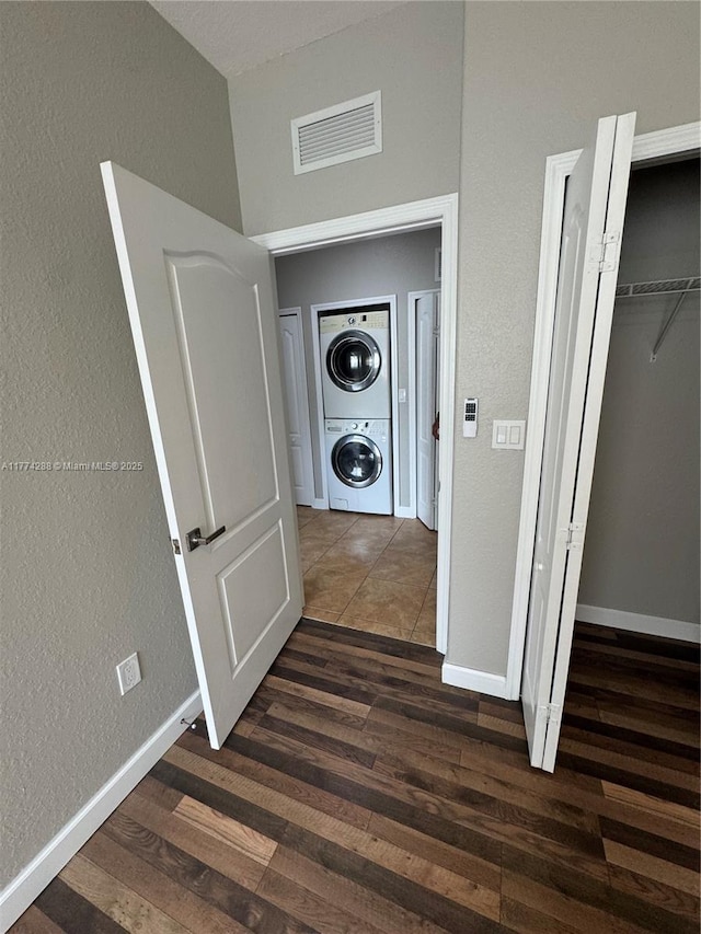 hallway featuring stacked washer and dryer, dark wood-style flooring, visible vents, and baseboards