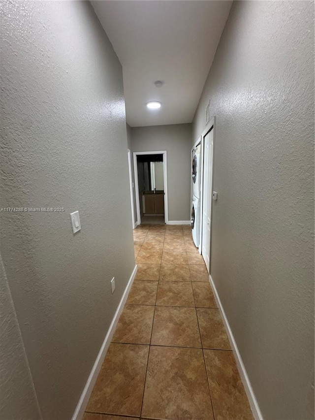 hall with tile patterned floors, a textured wall, stacked washer / drying machine, and baseboards