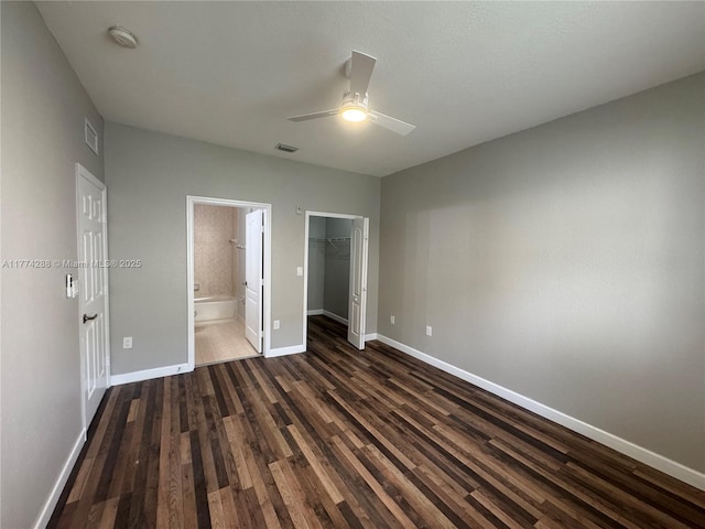 unfurnished bedroom featuring a closet, a walk in closet, baseboards, visible vents, and dark wood-type flooring