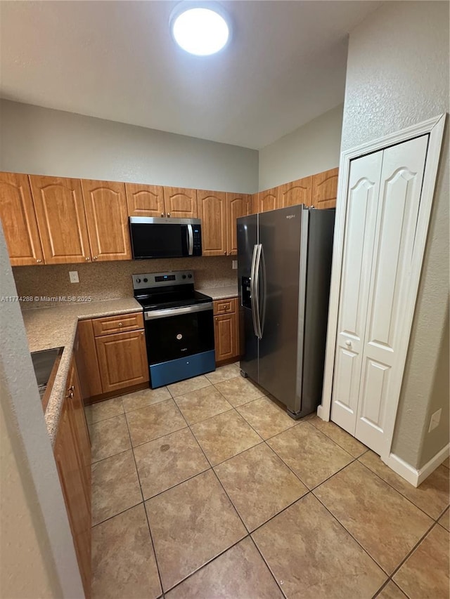 kitchen with light countertops, tasteful backsplash, light tile patterned flooring, appliances with stainless steel finishes, and brown cabinets