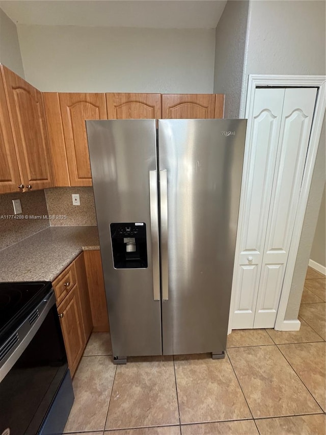kitchen with tasteful backsplash, brown cabinets, light tile patterned floors, electric range, and stainless steel refrigerator with ice dispenser