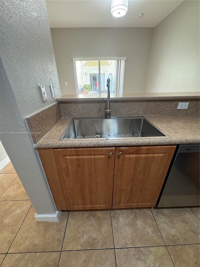 kitchen featuring light tile patterned floors, a sink, brown cabinetry, and stainless steel dishwasher